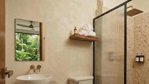 Un baño con lavamanos blanco, inodoro y zona de ducha con puerta de cristal.