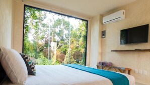 Un dormitorio con cama, televisor montado en la pared y un ventanal con vistas a zonas verdes.