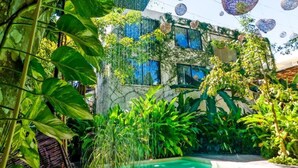 Un edificio con piscina, rodeado de vegetación exuberante y decoraciones esféricas colgantes.
