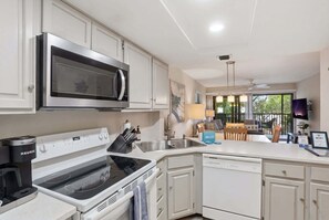 A modern kitchen with a microwave, stove, and dishwasher. There is a dining area with a table and chairs. - H-245 - Second Floor with Lake View -Sleeps 6 (Naples)