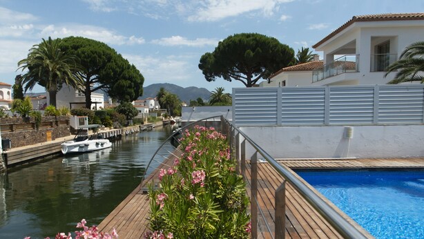 Ein Wohnhaus am Wasserufer mit Pool, einer Holzterrasse und Blick auf das Gewässer.
