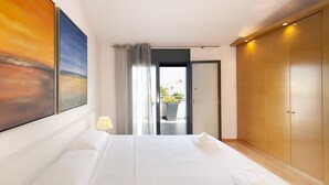 Ein Hotelzimmer mit einem großen Bett, Blick durch eine geöffnete Tür und einem Gemälde an der Wand.