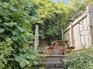 Ein Garten mit einer hölzernen Konstruktion, einem Metallgitter und dichtem Grün.