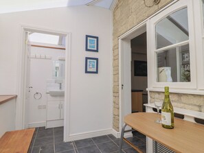 Una cocina con ventana, una mesa con una botella y una puerta que da a un baño.