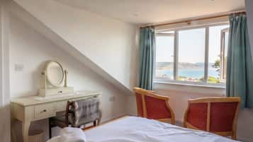 A bedroom with a bed, a dresser with a mirror, two chairs, and a window with curtains.