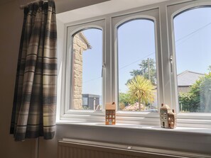 A window with two small houses on the sill, a curtain, and a stone wall outside. - Seaview (Lyme Regis)