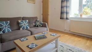 A living room with a brown sofa, a wooden coffee table, and a window with curtains. - Seaview (Lyme Regis)