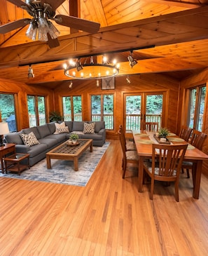 Ein Interieur einer Hütte mit einer Couch, einem Couchtisch, einem Esstisch, Stühlen und einem Deckenventilator.