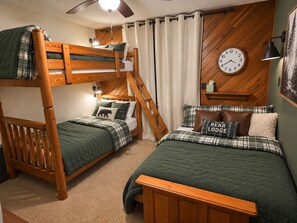 Ein Schlafraum mit Etagenbett, einem Holzlager, einem Nachttisch, einer Wanduhr und einem Bett mit einem Kissen, das 'BEAR LODGE' sagt.