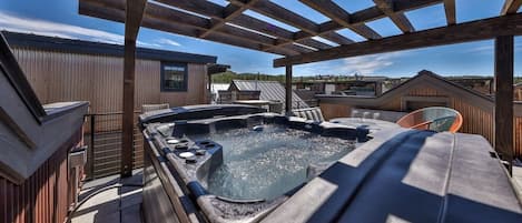 Un jacuzzi bajo una pérgola de madera con vista a edificios cercanos.