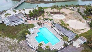 Ovenfra et resort med en central swimmingpool, omgivet af liggestole, et strandområde og en mole, der strækker sig ud i vandet.