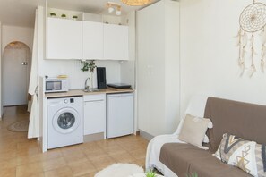 Een ruimtelijk ingerichte leefruimte met een wasmachine, een magnetron en een klein kitchenette.