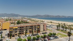 Ein mehrstöckiges Gebäude mit Parkplatz, Strand und Bergen im Hintergrund.