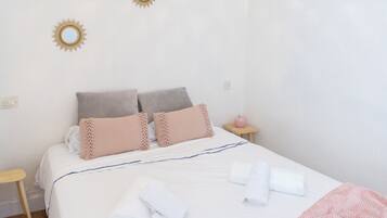 Una cama bien hecha con almohadas, una mesita de noche con una lámpara rosa y un espejo en la pared.