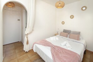 Een slaapkamer met een bed, kussens, een nachtkastje, een lamp en een spiegel aan de muur.