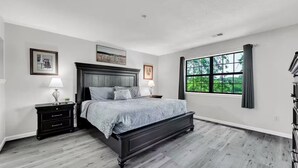 Une chambre à coucher avec un lit, des tables de chevet, une fenêtre avec des rideaux et une vue sur la verdure à l’extérieur.
