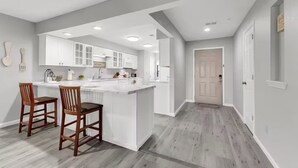 Une cuisine moderne avec des meubles blancs, un îlot central et deux chaises en bois.