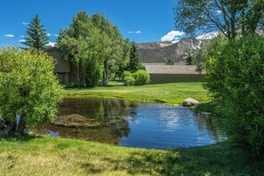 A serene outdoor setting with a pond, lush greenery, and a mountain backdrop. - Charming Snowcreek Meadow Unit w/ Views (Mammoth Lakes)