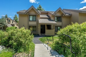 A two-story residential building with a covered front porch, a visible staircase leading to the entrance, and a pathway leading to the front door. - Charming Snowcreek Meadow Unit w/ Views (Mammoth Lakes)
