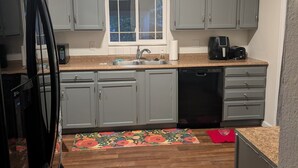 A compact kitchen with grey cabinets, a window, a sink, a coffee maker, and a dishwasher. - Fabulous 3-bedroom duplex in friendly Greeley (Greeley)