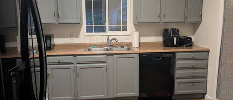 A compact kitchen with grey cabinets, a window, a sink, a coffee maker, and a dishwasher.