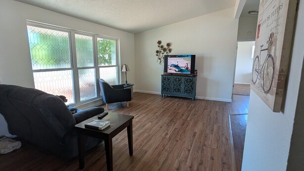 A living room with a sofa, a coffee table, a TV on a cabinet, and a large window with a view of greenery. - Fabulous 3-bedroom duplex in friendly Greeley (Greeley)