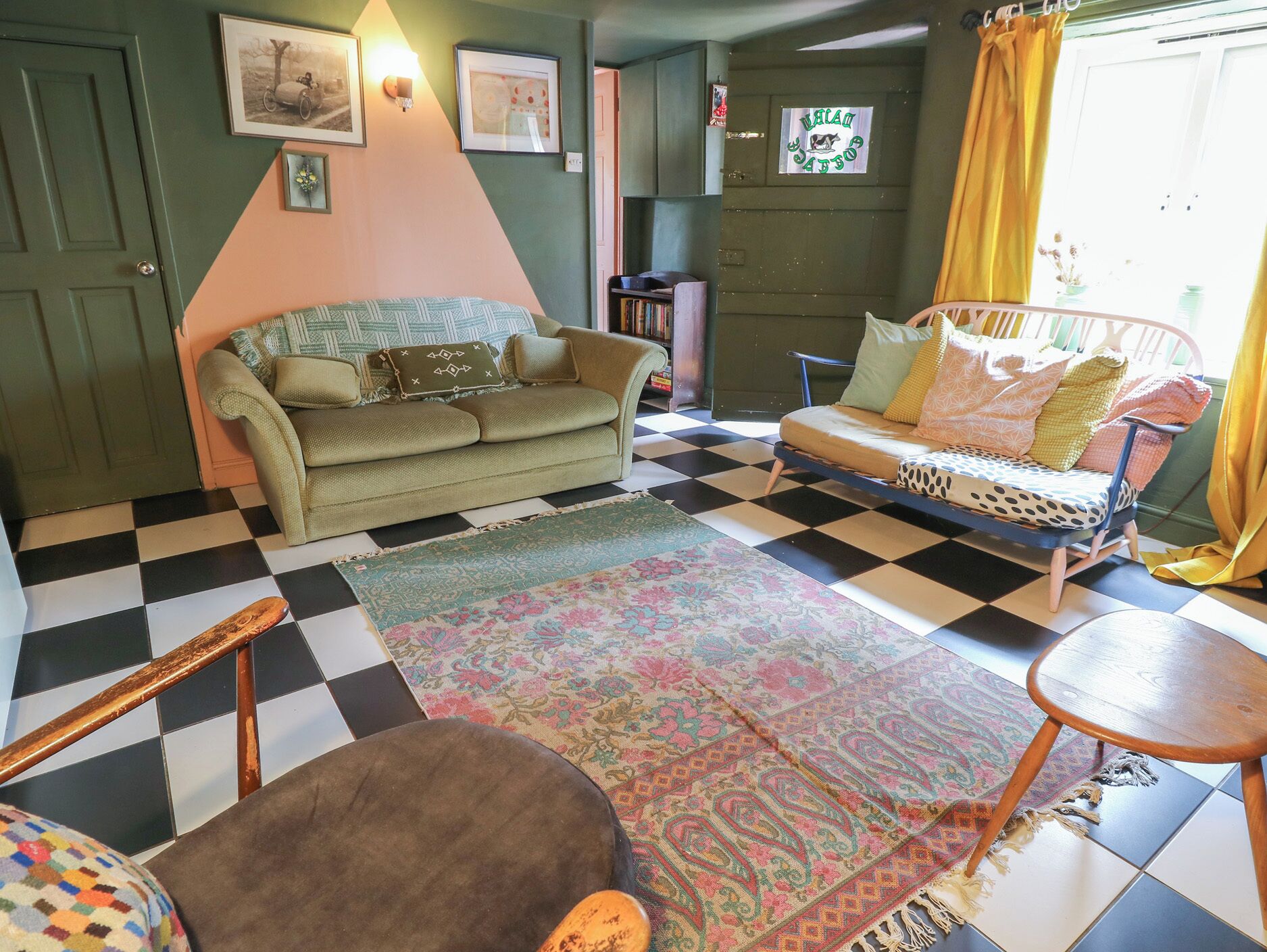 A room with a checkered floor, a green sofa, a patterned rug, and a bed with a polka dot cover.