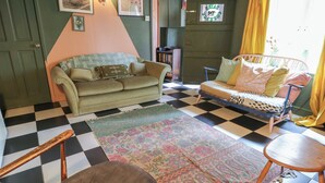 A room with a checkered floor, a green sofa, a patterned rug, and a bed with a polka dot cover. - Dairy Cottage (Ventnor)