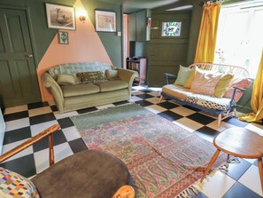 A room with a checkered floor, a green sofa, a patterned rug, and a bed with a polka dot cover. - Dairy Cottage (Ventnor)