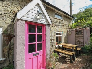 A stone house with a pink door, a small wooden bench, and a hanging plant. - Dairy Cottage (Ventnor)