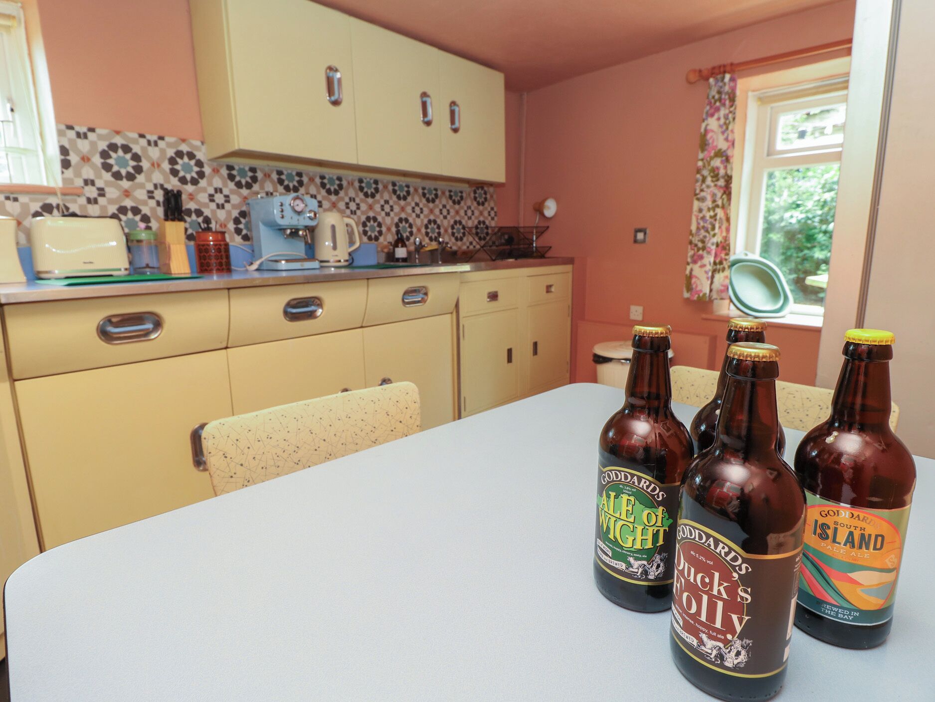 A kitchen with a table displaying bottles of beer, a toaster, and a kettle.