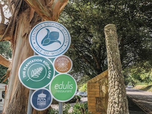 A sign with multiple logos including 'Entor Botanica Garden Isle of Wight,' 'The Plantation Room Cafe,' 'Wellbeing Classes,' 'Edulis Restaurant,' and 'Puya Boutique Shopping.' - Dairy Cottage (Ventnor)
