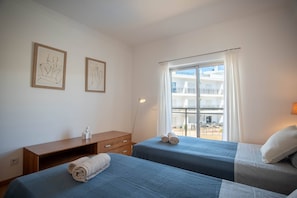 A hotel room with two beds, a desk, and a window with a view of a balcony. - Albufeira 2-Bedroom Apartment w/ Pool, Sauna & Gym (Albufeira)
