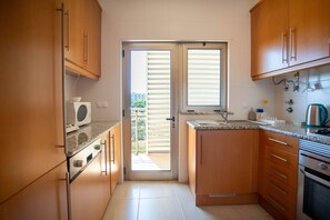 A compact kitchen with wooden cabinets, a built-in oven, a microwave, and a sink. - Albufeira 2-Bedroom Apartment w/ Pool, Sauna & Gym (Albufeira)