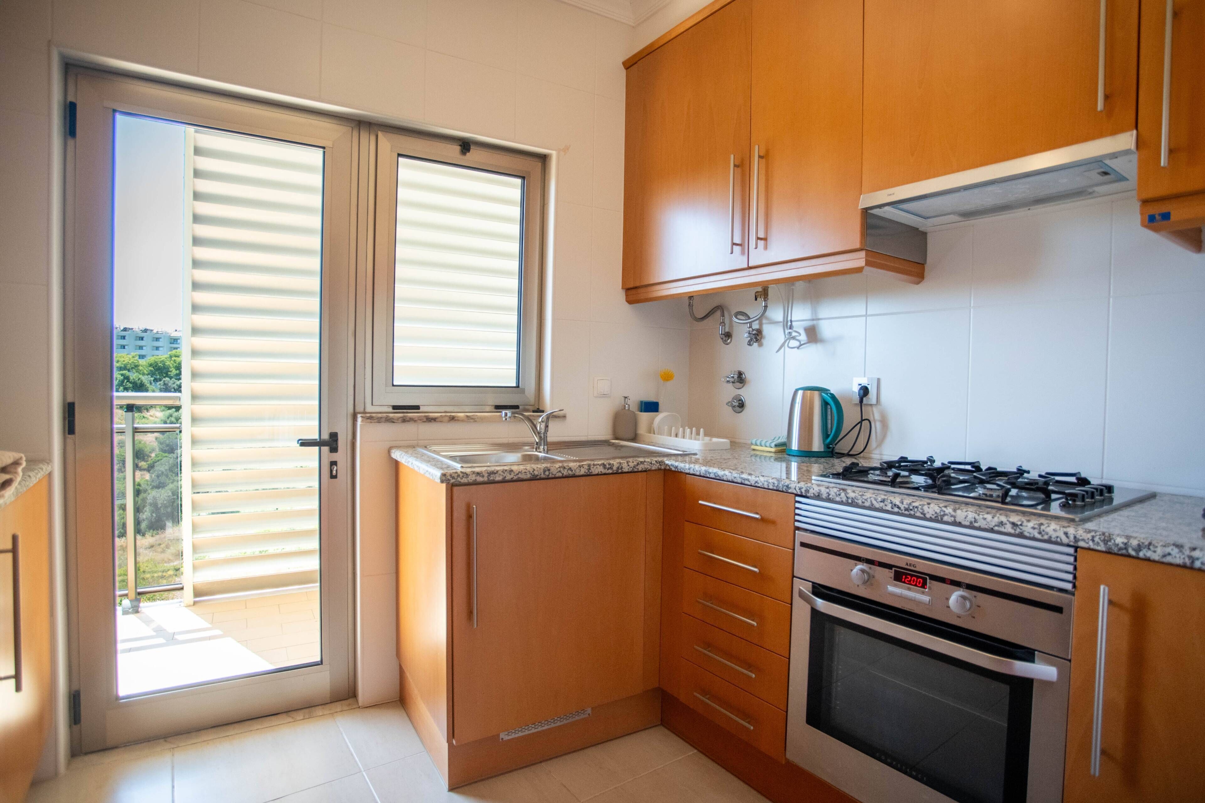 A compact kitchen with wooden cabinets, a built-in oven, and a window with blinds.