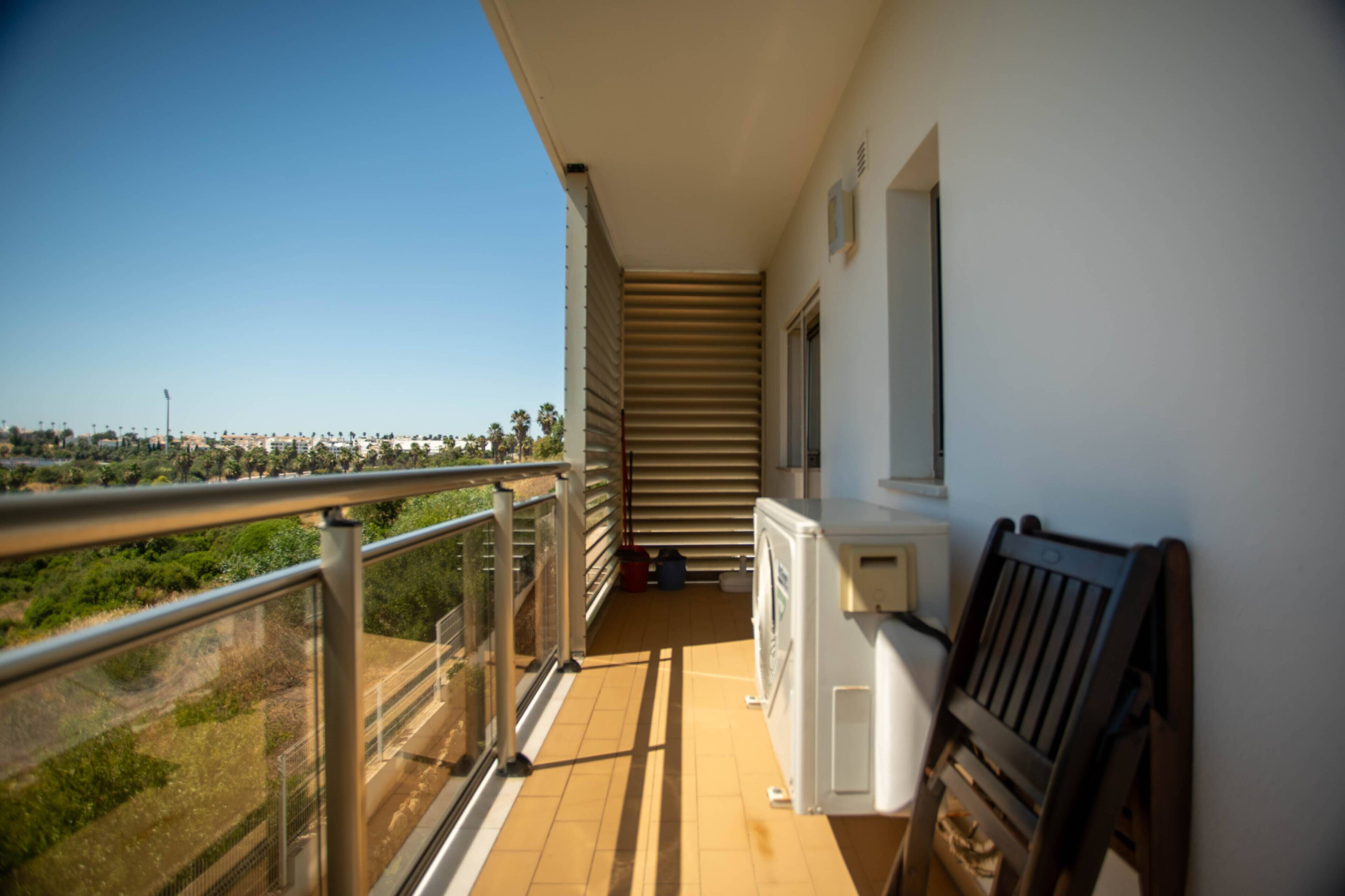 A balcony with a view of a cityscape, a washing machine, and a bench.