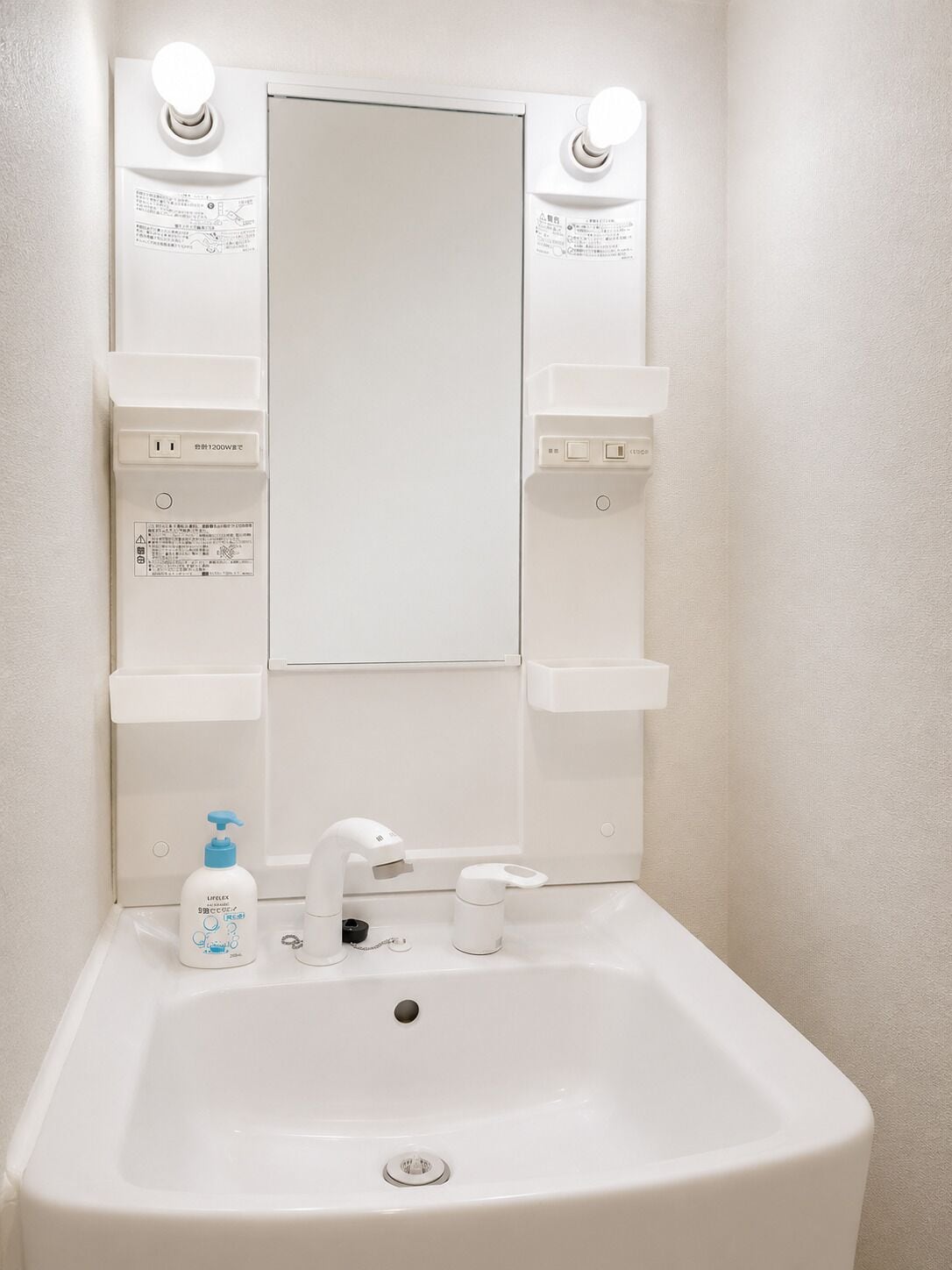 Un baño con lavamanos blanco, espejo y dos apliques de luz.