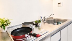 Eine Küche mit Herd, Spüle, einer roten Bratpfanne, einem kleinen Topfpflanzen und einer Handseifenflasche.