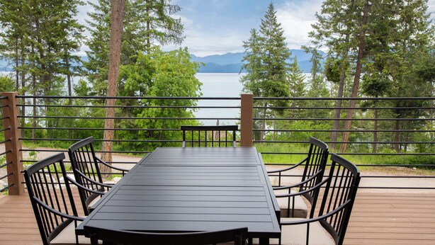 A deck with a table and chairs, overlooking a lake and mountains.