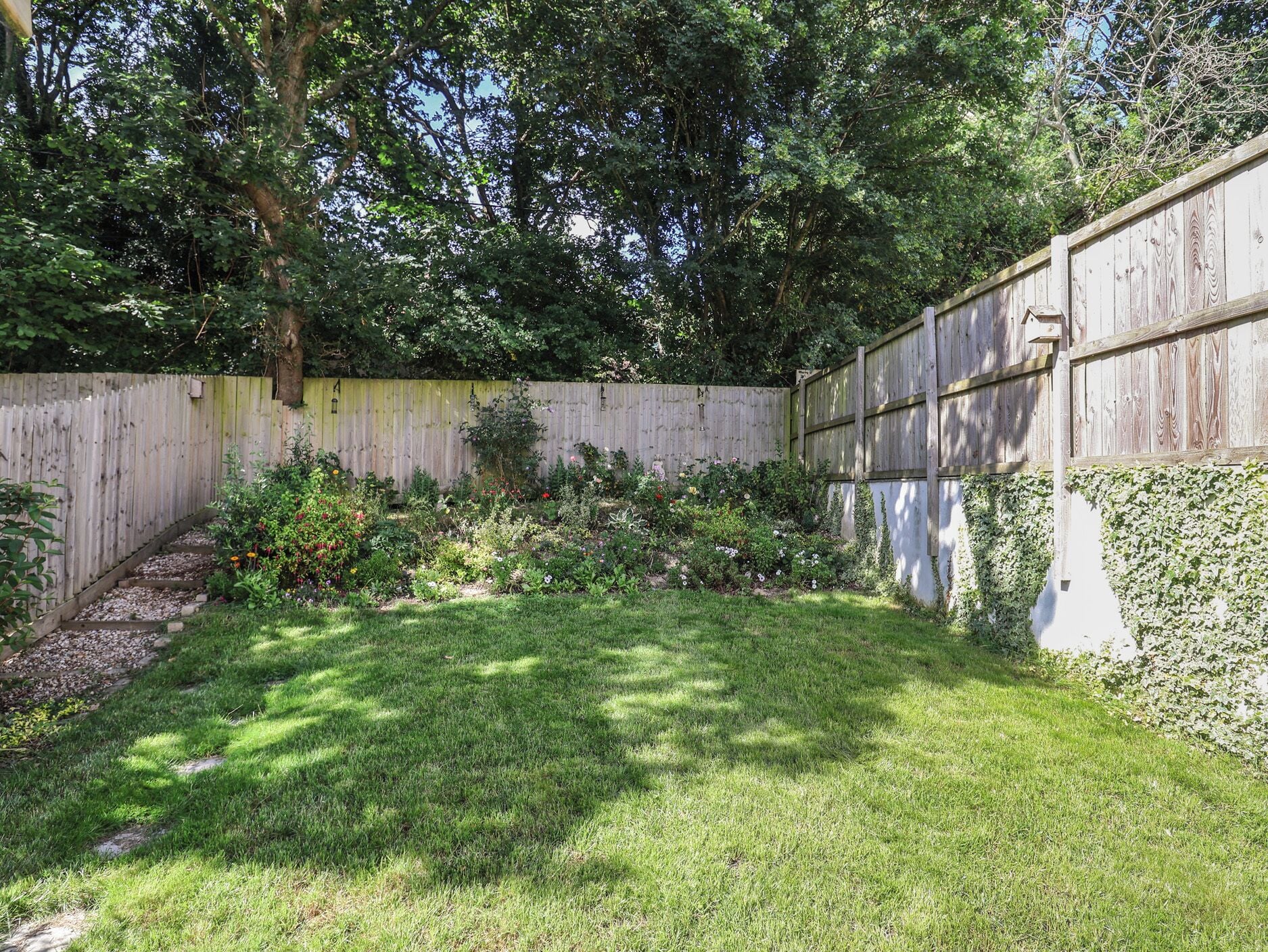 A backyard with a wooden fence, a grassy lawn, and a variety of plants and flowers.