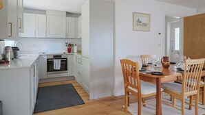 Cozinha moderna com armários brancos, uma mesa de jantar para quatro pessoas e um forno pequeno.