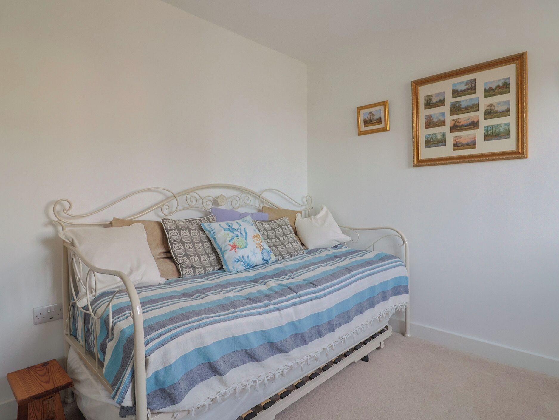 A single bed with a metal frame, a striped blanket, and several pillows. There is a small wooden stool beside the bed.