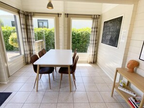Ein Zimmer mit weißem Tisch und Stühlen, großen Fenstern mit Vorhängen, einer Tafel mit Schrift und einem Holzregal mit Büchern und einem Büsten.