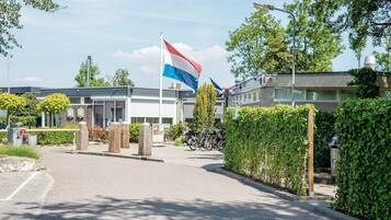 A building with a flag, a bicycle, and a hedge.