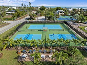 A tennis court complex with multiple courts, surrounded by palm trees and a view of the ocean. - Loggerhead Cay 584 Side Water Pool Views (Sanibel)
