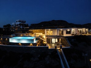 A modern villa with a swimming pool, outdoor seating, and a view of the surrounding landscape.