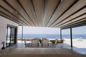 A modern interior with a view of the ocean, a dining area with chairs and a table, and a glass door leading outside.