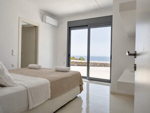 A bedroom with a bed, a sliding glass door to a balcony, and an air conditioning unit.