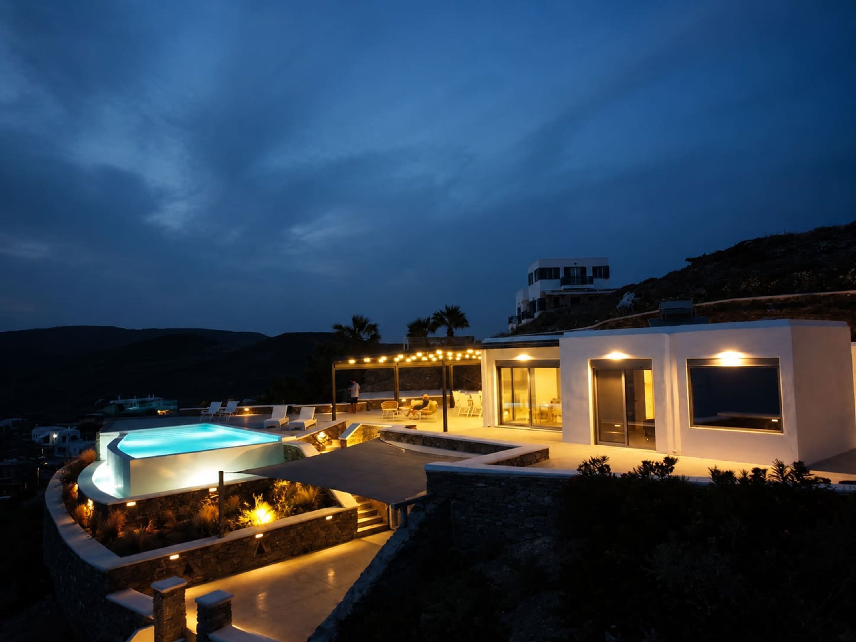 A modern villa with a swimming pool, outdoor seating, and a view of the surrounding landscape.
