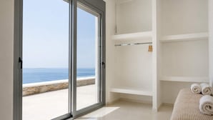 A room with a large sliding glass door leading to a balcony with a view of the sea. There are white shelves and a rolled towel on the floor. - Kythnos Luxury Villa Aegean View Private Pool Gem (Kithnos)